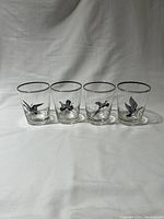 Full set of four clear glass cocktail glasses with black game bird illustrations and silver rims, lined up side by side on a white surface and background.