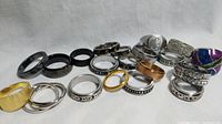 Overview of 20 assorted metal rings showing various finishes and styles including gold tone, silver, black enamel, and spinner rings with patterns.