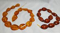 Two strands of amber beads, one lighter and one darker, laid side by side showing shape and color differences.