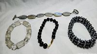 Four semi precious stone bracelets including moonstone, quartz crystal, black onyx, and hematite laid out on white surface.