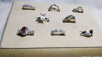 Overall view of 8 silver tone rings with various semi precious stones arranged on a beige display pad