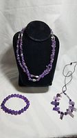 Amethyst chip strand necklace displayed on a black jewelry bust, round amethyst bead bracelet beside it, and Native American style amethyst fetish necklace with leather cord