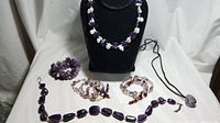 Full view of all jewelry items including necklaces, bracelets, and cluster amethyst stone on white background with display stand