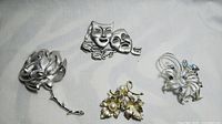 Four jewelry pins displayed on a plain white background showing mixed metal tones including silver and gold-tone pieces.