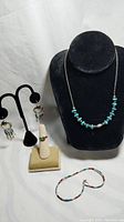 Photo of the entire Navajo jewelry set including earrings on black stand, silver and turquoise bead necklace on bust, ring on stand, multi-colored bead bracelet.