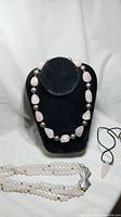 Display of a rose quartz necklace with large polished teardrop-shaped stones and round sterling silver beads on a black stand, with other necklaces partially visible.