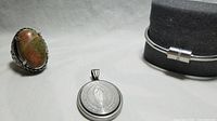 Jewelry lot arranged showing oval religious medallion, bracelet on display stand, and large semi-precious stone ring.