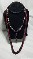 Full view of two necklaces on black display, showing the long garnet rope and necklace with silver pearls and pendant.