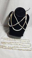 All three necklaces displayed on black necklace bust. Three strands shown: sterling silver mesh chain, white pearl strand, multicolor pearl and stone strand.