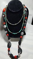 Three layered necklaces featuring turquoise barrel beads, black pearls, lava stones, coral and Murano glass beads on black necklace display stand.