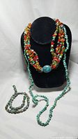 Overall view of three pieces of turquoise chip and red Mediterranean coral chip necklaces displayed on a black stand and table.
