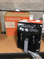 Cosori Pro Gen 2 5.8 Quart Smart Air Fryer box and air fryer unit wrapped in plastic with handle visible on shelf