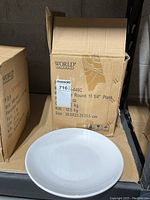 Box of World Tableware branded plates with open box showing one white round plate in front.