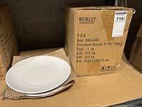 Photo of the box labeled World Tableware with 12 round porcelain plates. Shows the front of the box and partially exposed plates inside.