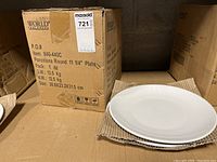 View of the original box labeled World Tableware with stack of white plates in front.
