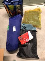 Full view of all four items in the lot including tent bag, yellow mesh tarp bag, black drawstring bag with mattress, and boxed air pump.