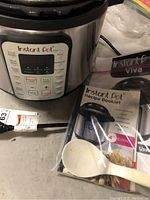 Front view of Instant Pot Viva with control panel and included recipe booklet and spoon in packaging.