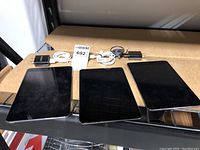 Front view of three Apple iPad Mini tablets showing black screens and home buttons, with three chargers behind them.