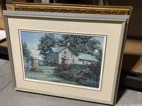 Framed and matted print showing a stone house scene with garden and wall, overall view with frame and matting.