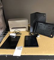 Samsung Galaxy Tab A7 Lite tablet, its original box, USB charger, and protective case alongside Amazon mini tablet with charger and protective case on cardboard surface.