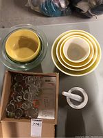 Top-down view of the lot showing 11 small clip-lid spice jars in a box, yellow and clear glass bowls, and a white marble mortar and pestle with pestle inside.