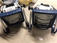 Two white metal framed Regent work lights with blue protective grill fronts and black grills covering glass lenses, placed side by side showing front view.