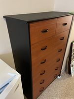 View of the highboy dresser showing black top and sides with wood-colored drawer fronts and black handles.