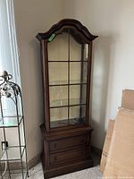 View of entire display cabinet showing dark wood finish, glass door with grid pattern, and base with drawers.