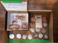 Six silver rounds in a cigar box, including two in plastic flips and four loose rounds