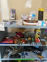 Shelving unit with two shelves holding various hand tools, packaged hardware items, and miscellaneous construction accessories.