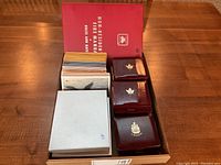 Box containing approximately 56 white PL folders and six burgundy clamshell cases embossed with Maple leaf and Canada crest