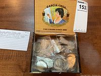 Wooden table with an open Garcia y Vega cigar box containing individually sleeved Canadian silver dollars.