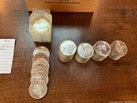 Stacks of uncirculated Canadian silver dollars and a plastic coin tube on wooden surface