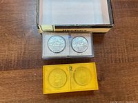 Four silver dollar coins in two coin flips, two in a clear plastic 2-coin flip and two in a yellow plastic block