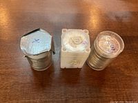 Three plastic coin tubes holding silver dollars: one aluminum-sealed tube, one white four-sided tube, one clear round tube