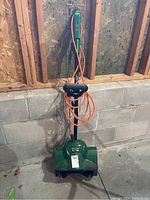 Full front view of the green Certified electric snowthrower showing handle, auger area and extension cord.