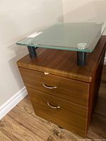 Image showing front and right side of cabinet with glass top and handles on drawers.