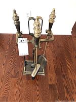 Full view of the brass fireplace tool set in the stand on hardwood floor