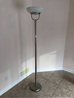 Full view of the tall floor lamp with round base and upward-facing white glass shade.