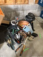 Garden lot items laid out including rusty tomato cages, plastic and terracotta planters, assorted garden hand tools, and hose attachments.