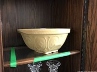 Mustard yellow ceramic mixing bowl on wooden shelf showing side profile and decorative pattern.