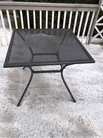 Square metal patio table front view showing mesh top and legs.