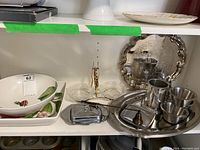 Photo showing ceramic serving dishes with floral design, metal butter dish with lid, small ramekins and pewter mug, along with trays in background