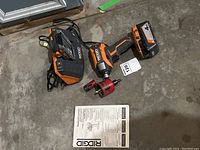 Ridgid drill, both batteries, charger, and manual arranged on floor for full lot view