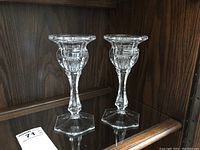 Pair of clear glass Royal Doulton candle holders on a glass shelf with auction tag.