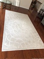 Full view of beige rug with abstract textured geometric pattern laid on wooden floor.