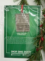 Front of package showing pewter ornament and historical information about Cooke's Fine Foods at 61 Brock Street, Kingston.