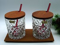 Front view of two crystal tumblers on teak tray with lids and red spoons in place