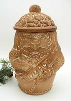 Front view showing the figure's face, embossed text, and fruit-themed lid knob.