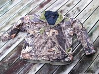Front view of the Mossy Oak camouflage jacket laid flat showing zipper, pockets, and collar with integrated neck warmer.